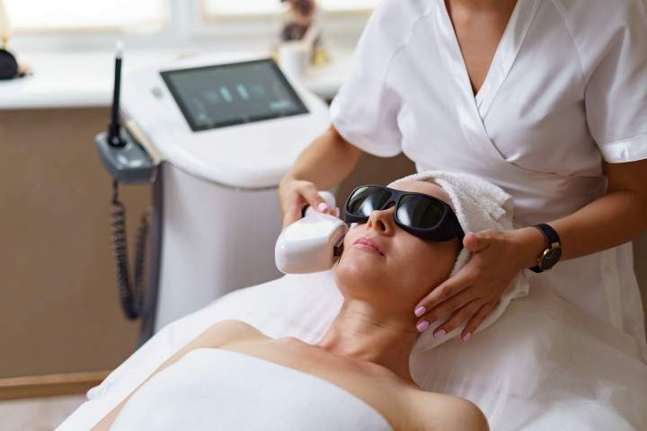 view doctor cosmetologist doing anti aging procedure cosmetology office satisfied woman disposable hat lying couch relaxing